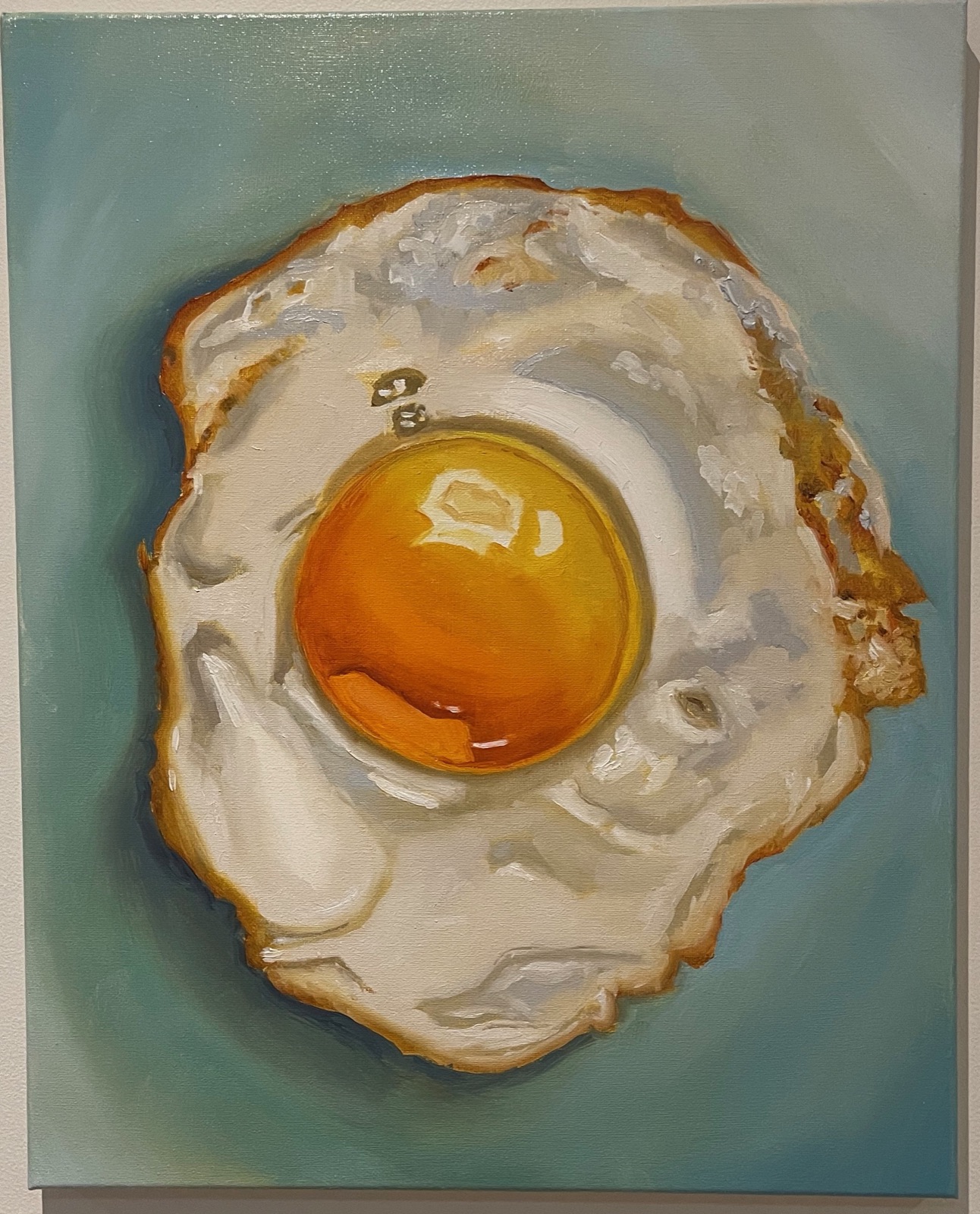 A fried egg painted on a pale blue canvas, the yolk glossy orange