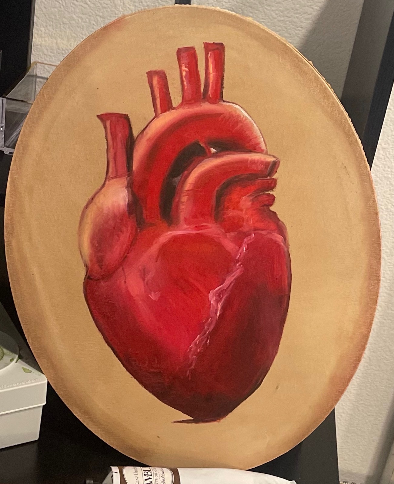 An anatomical heart painted in reds on a bare wooden oval panel