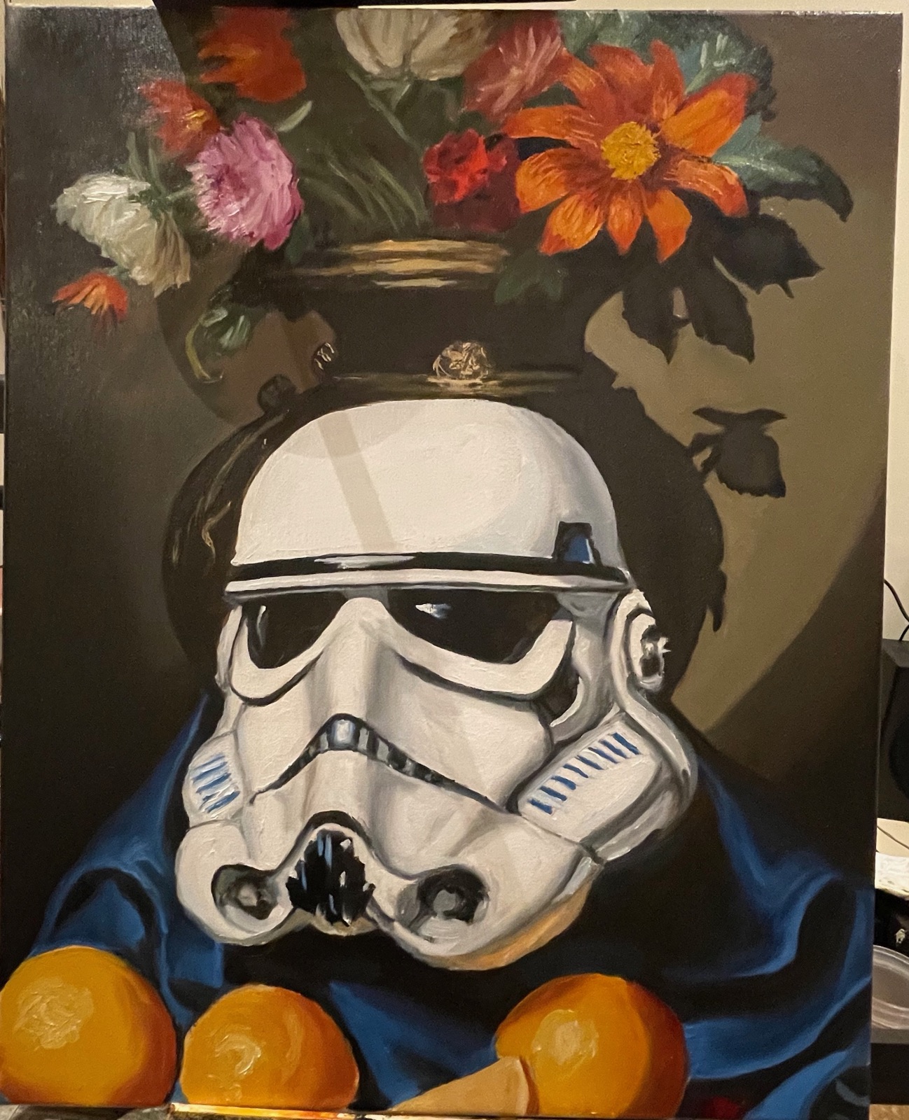 A stormtrooper helmet painted like a Dutch still life, a vase of flowers above it, oranges and blue cloth below, on the easel